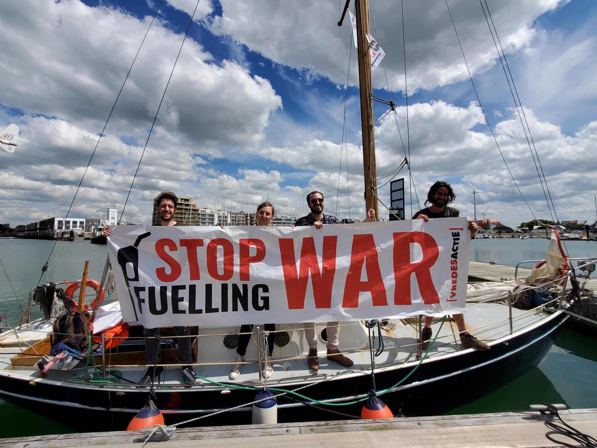 Vier mensen staan op een boot en houden een banner vast, waarop staat 'stop fuelling war'