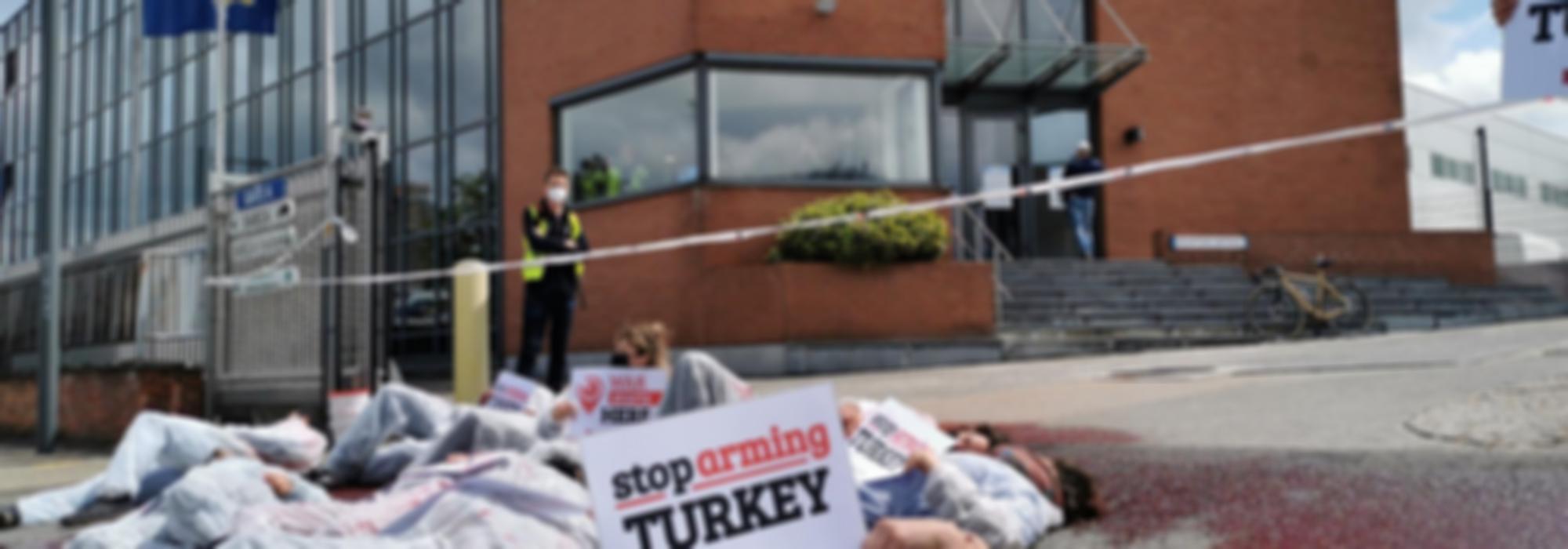 protest bij wapenfabrikant Sabca - mensen liggen op de grond in die-in. Iemand houdt bordje vast "Stop Arming Turkey"