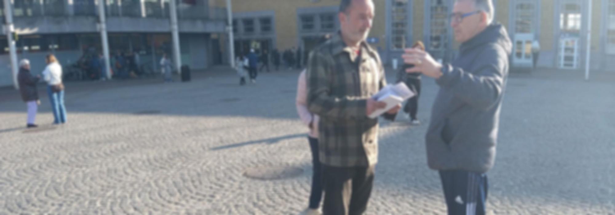Twee mensen praten over een brief op een zonovergoten plein
