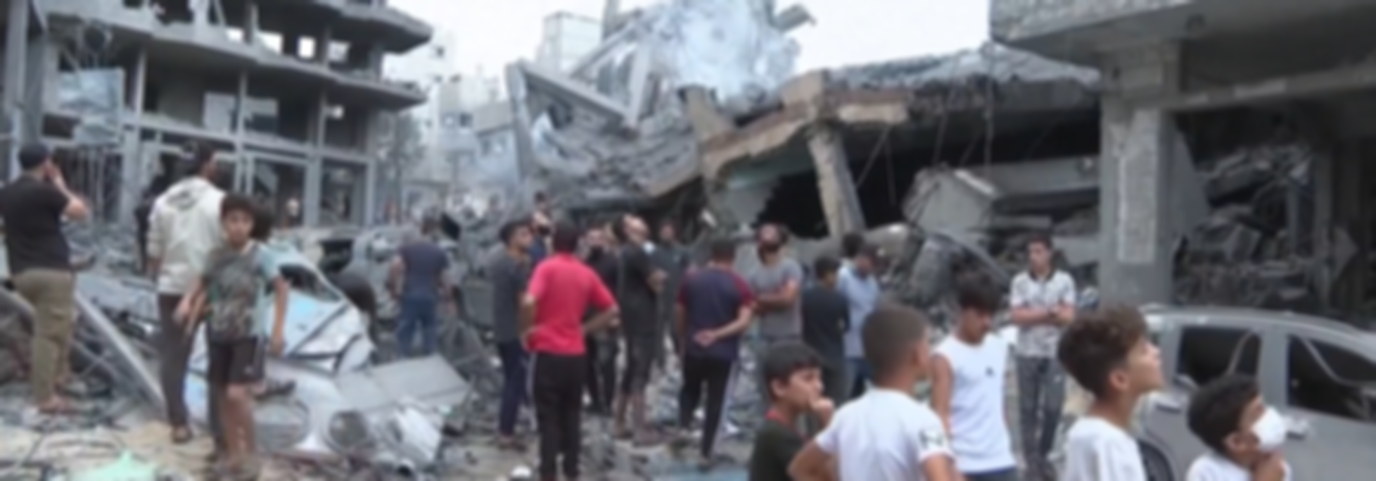 Mensen in Gaza staan in een verwoeste straat, omringd door verwoeste gebouwen.