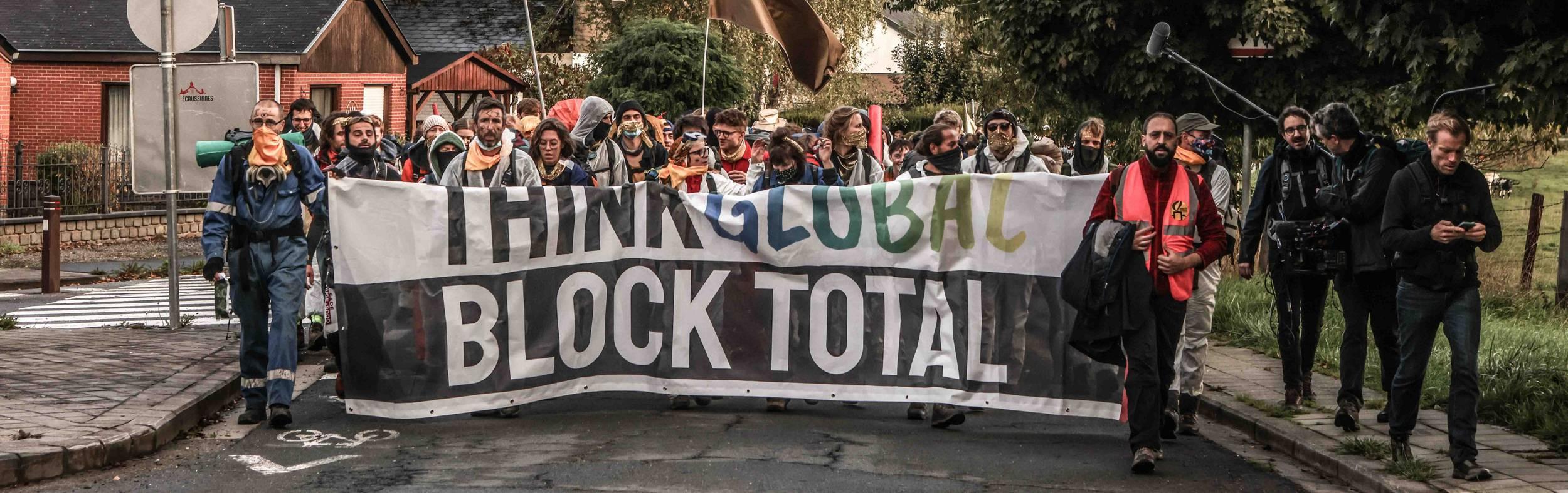 Een betoging in de straat. Op een spandoek staat "think global stop total"