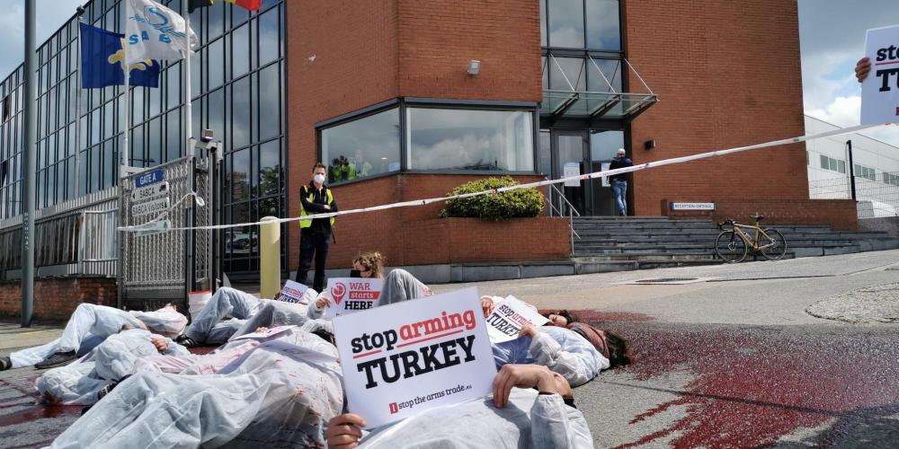 protest bij wapenfabrikant Sabca - mensen liggen op de grond in die-in. Iemand houdt bordje vast "Stop Arming Turkey"