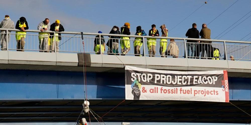 Activisten op een brug met spandoek 'stop project eacop & all fossil fuel projects'